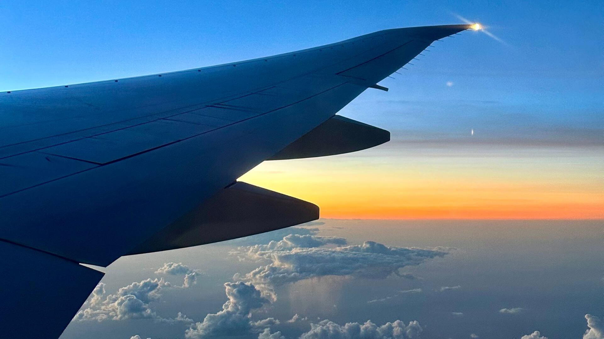 An airplane wing flying over the clouds during a sunset
